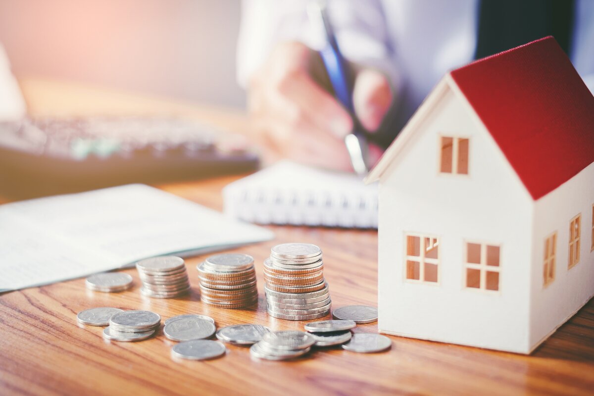 person making notes and using calculator on table next to model house with piled coins