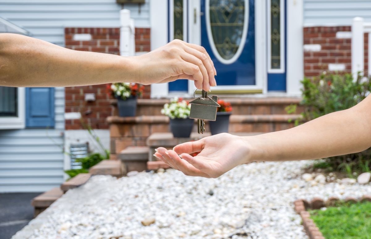 one hand handing over keys to another in front of new home